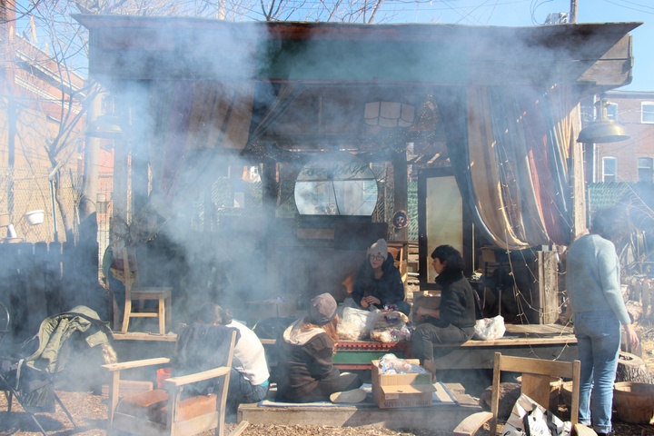 People sit in an open-sided shed, with a smoke surrounding them. 