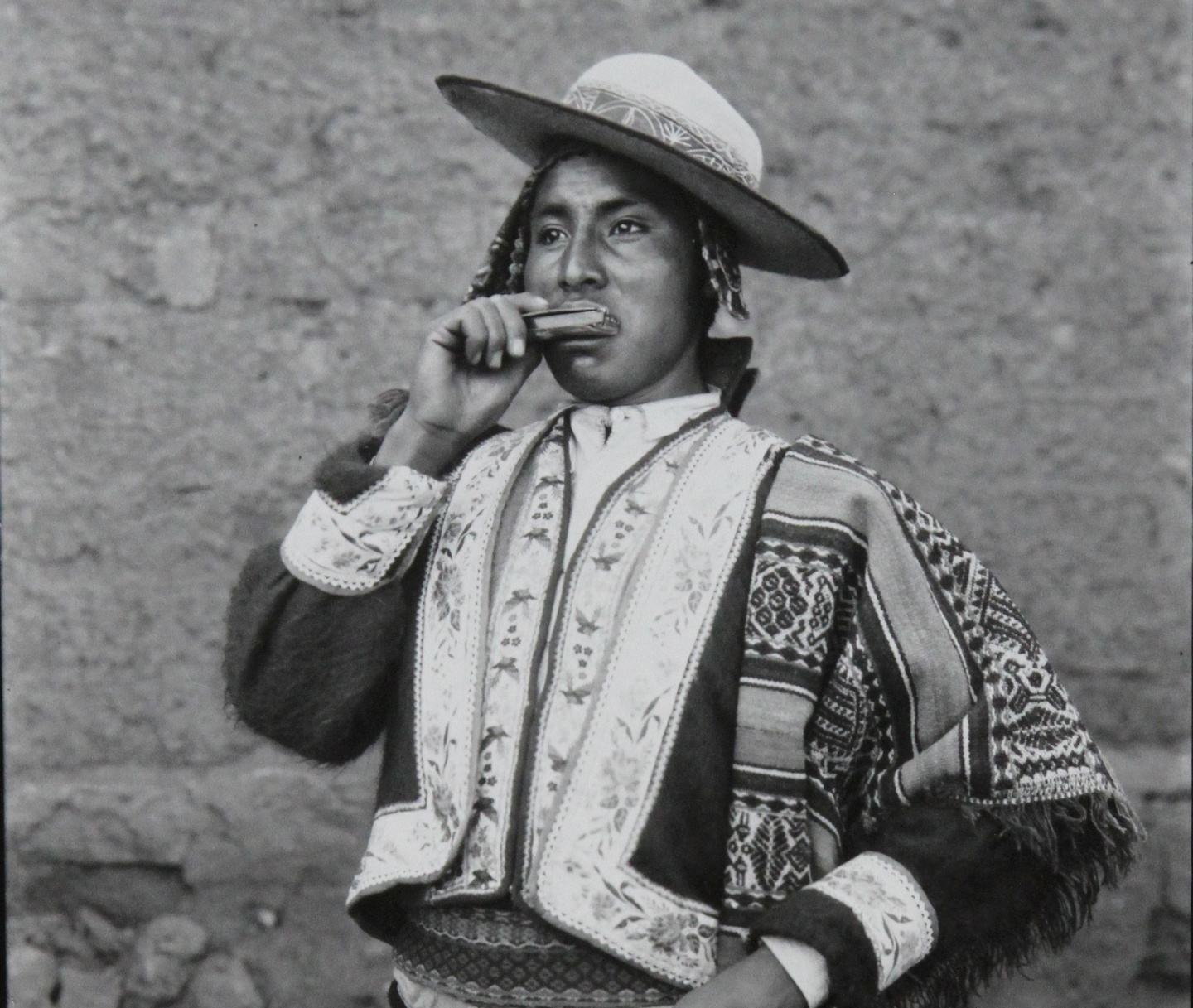 A photograph of a Peruvian man in indigenous dress blowing on a flute