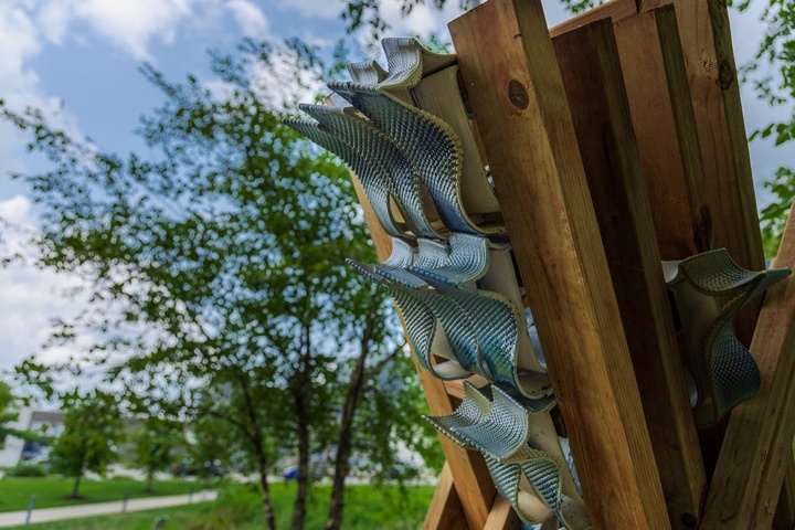 Detail of wood and ceramic sculpture with tree, grass, and blue sky with clouds in the background.