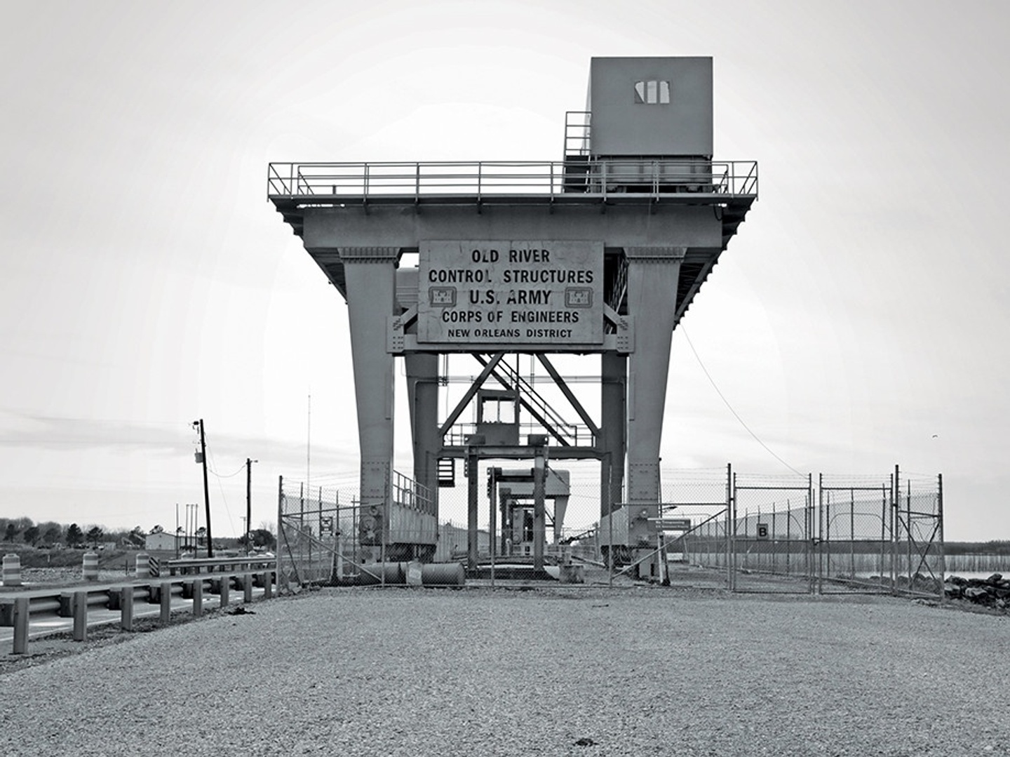 Black-and-white photo of a river control structure in New Orleans. The sign says, "Old River Control Structures U.S. Army Corps of Engineers New Orleans District."