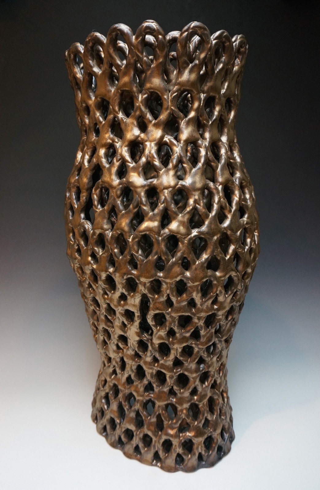 An intricately looped/patterned vessel, curving out slightly at the middle, in a rich golden-brown hue.
