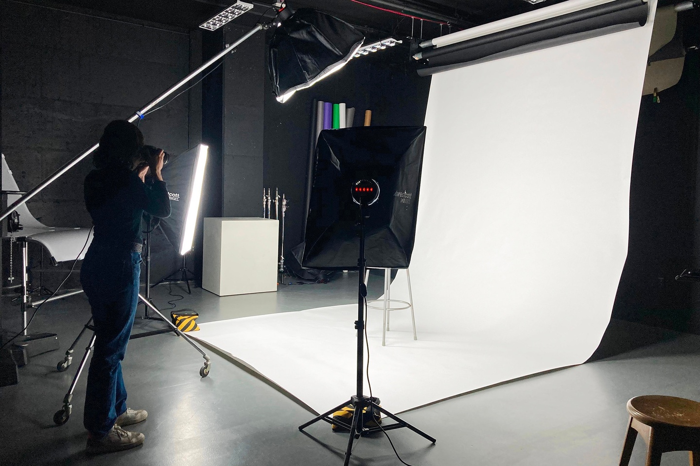 Person photographing work in the lighting studio, using special equipment such as an unfurled white backdrop and lights.