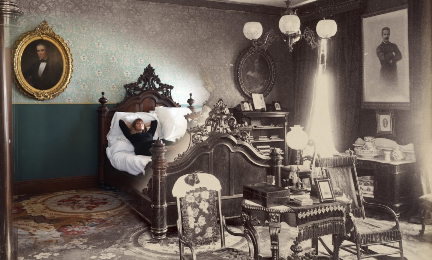 Image of an ornately decorated room that starts in full-color on the left and shifts to black-and-white as you pan across the image. Several framed portraits hang on the walls; an individual is lying down in an ornate bed in the middle of the room, with numerous chairs in front of it and a bookshelf and desk to the right.