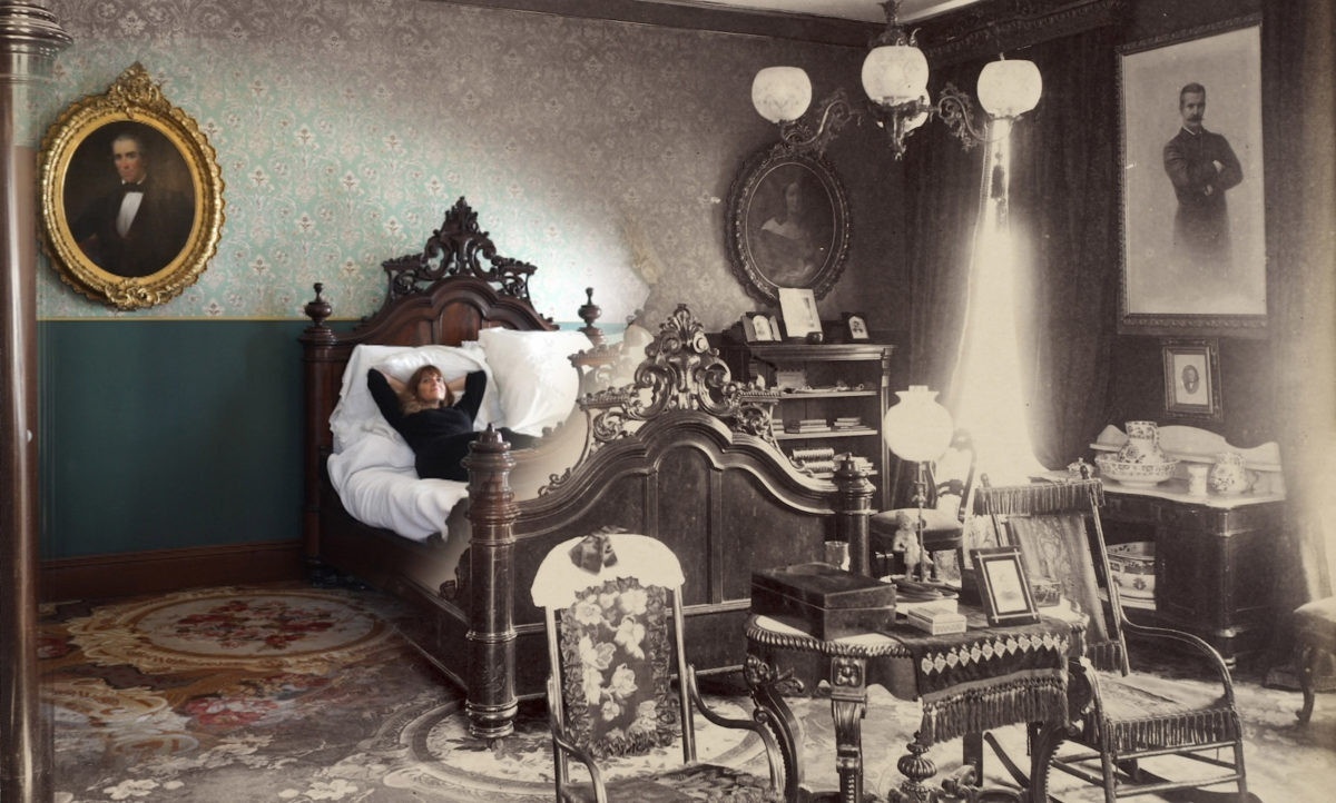 Image of an ornately decorated room that starts in full-color on the left and shifts to black-and-white as you pan across the image. Several framed portraits hang on the walls; an individual is lying down in an ornate bed in the middle of the room, with numerous chairs in front of it and a bookshelf and desk to the right.