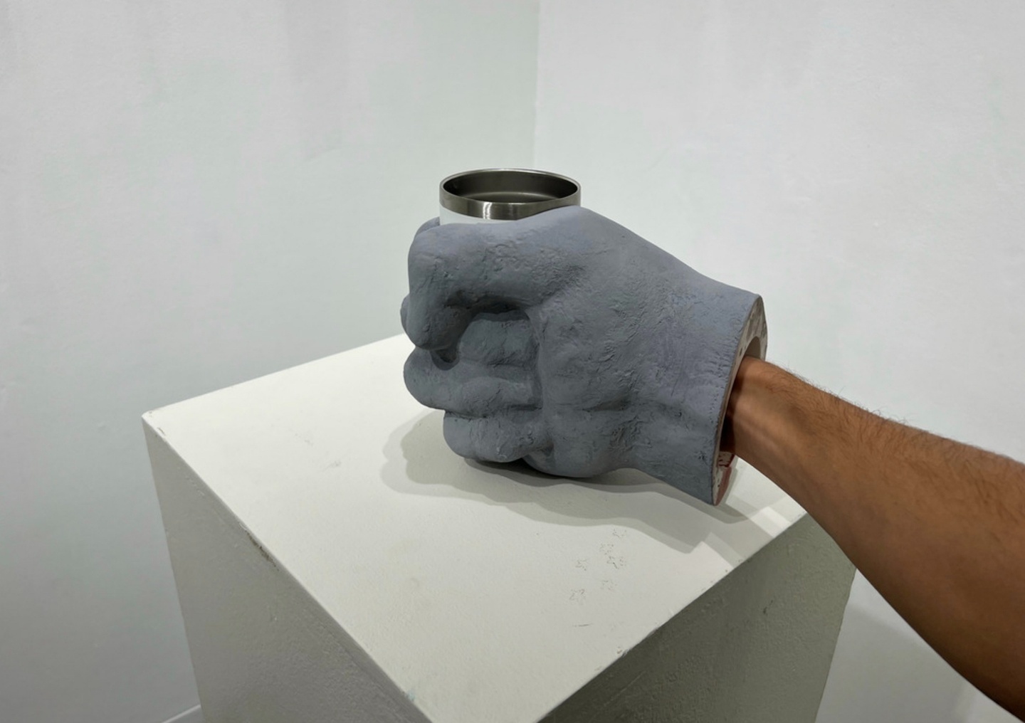 A large clay glove grasping a mug