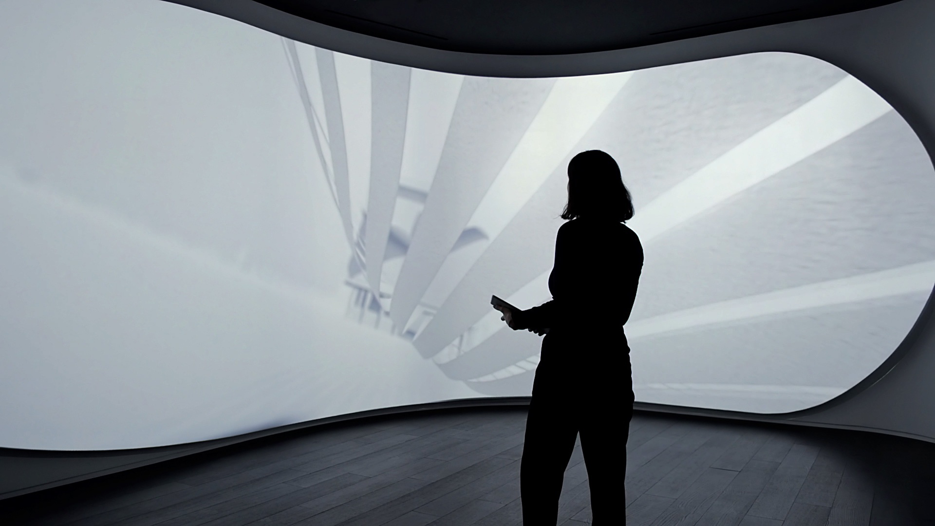 Woman holding a mobile device standing in front of a curved screen that displays architectural and graphic animations