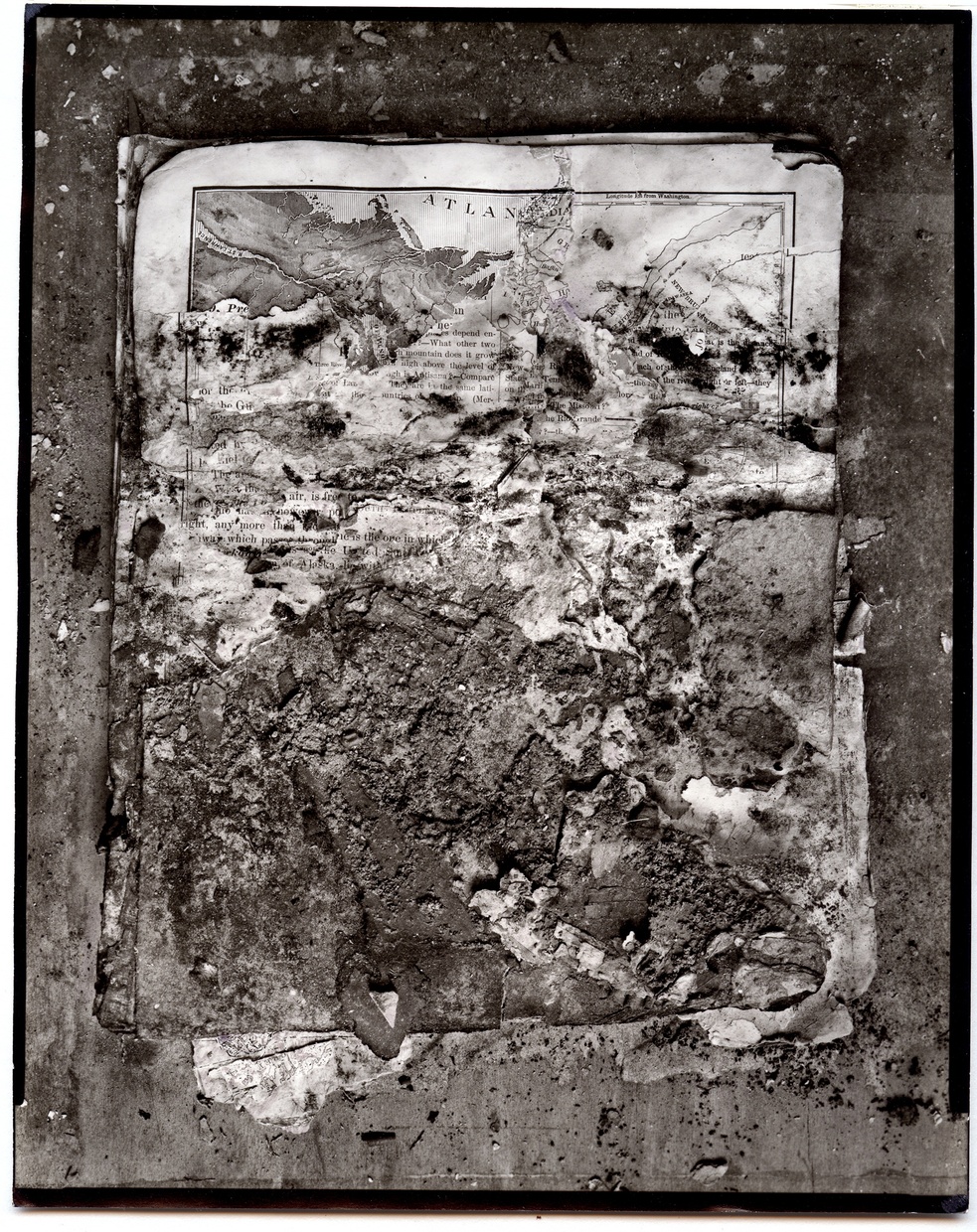 Black-and-white photograph of a stack of papers with text and a map visible, torn and covered with dirt and debris.