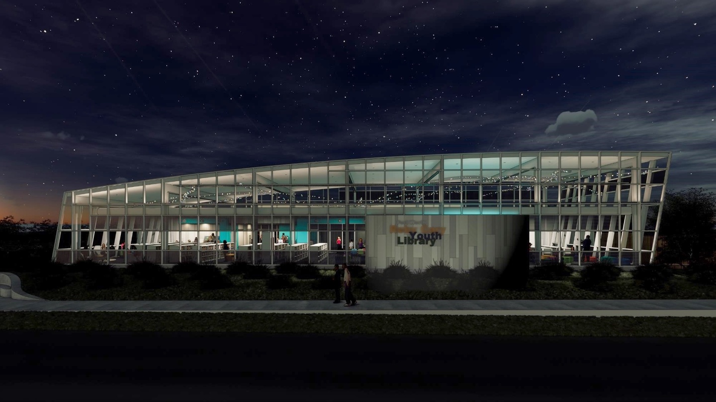 Evening photo of the exterior facade of a two-story children's library, with banks of floor-to-ceiling windows along most of both floors, except the first floor entry, and a gently sloped roofline.