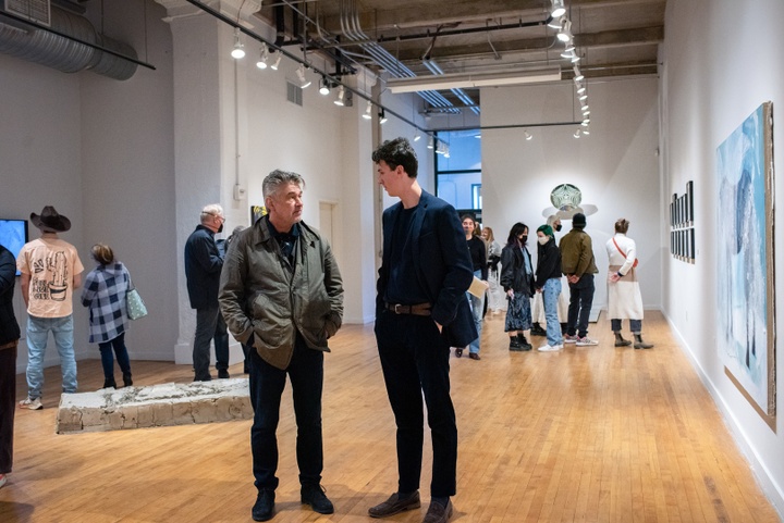 People fill a gallery space with both 2D and 3D work visible.