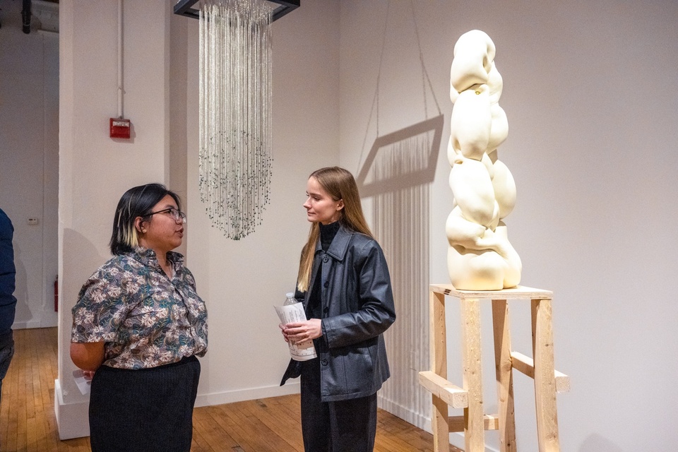 Two people stand next to a bulbous plaster sculpture on a wooden plinth.