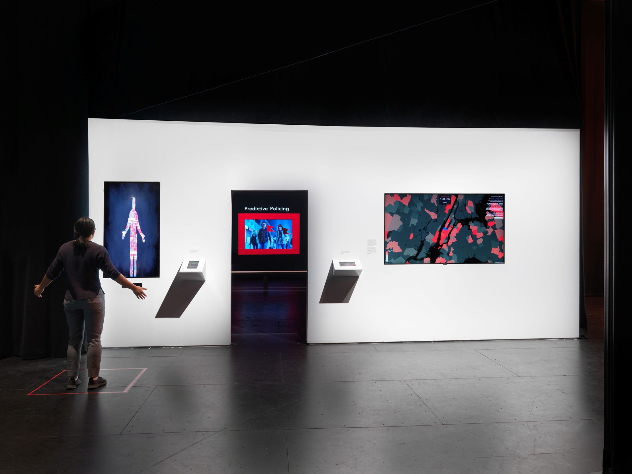 A photo of a video installation with a person standing with arms out in front of a video screen where the outline of their body appears