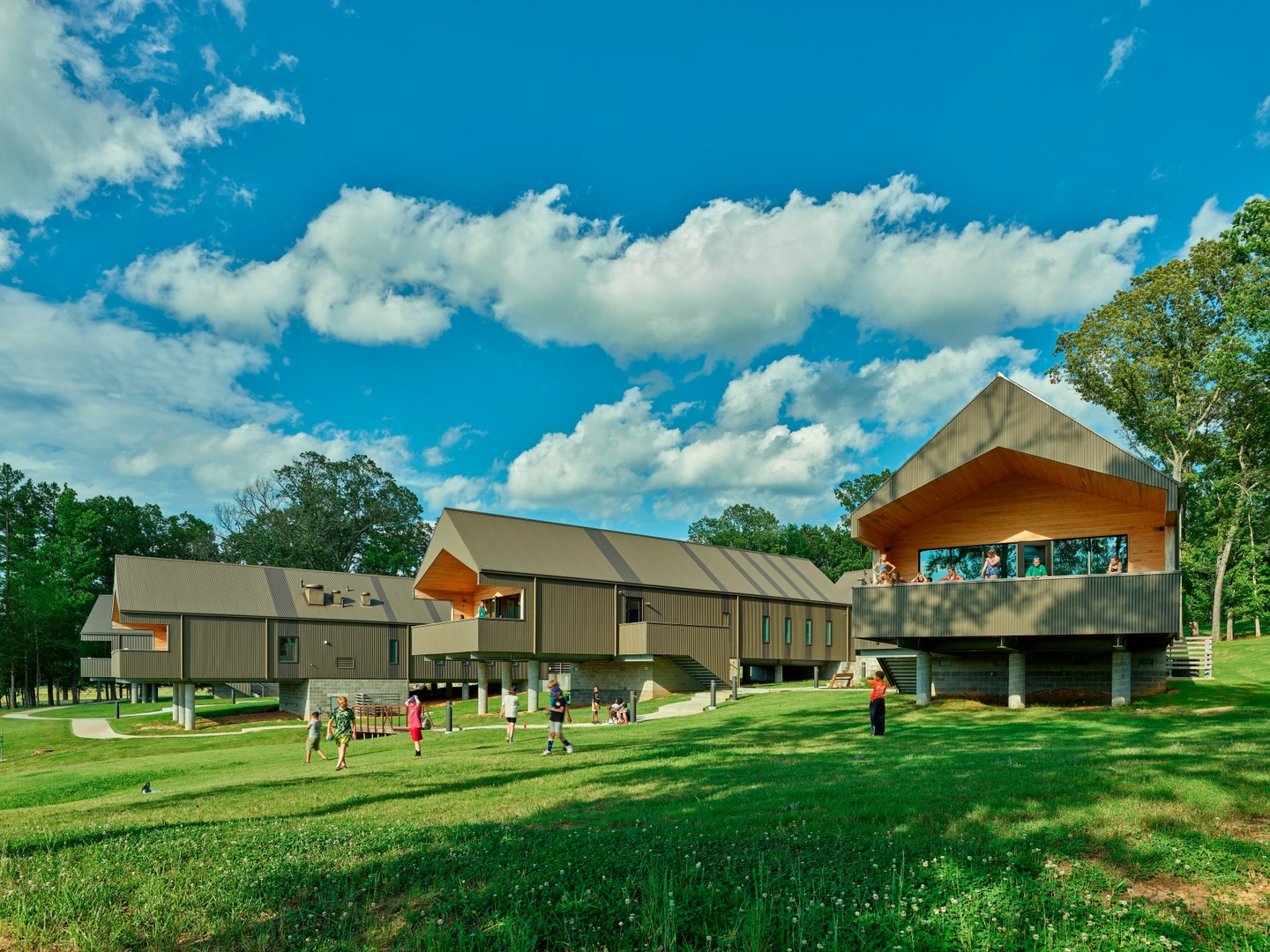 photo of a four long buildings on stilts on green grass with blue skies and people walking around