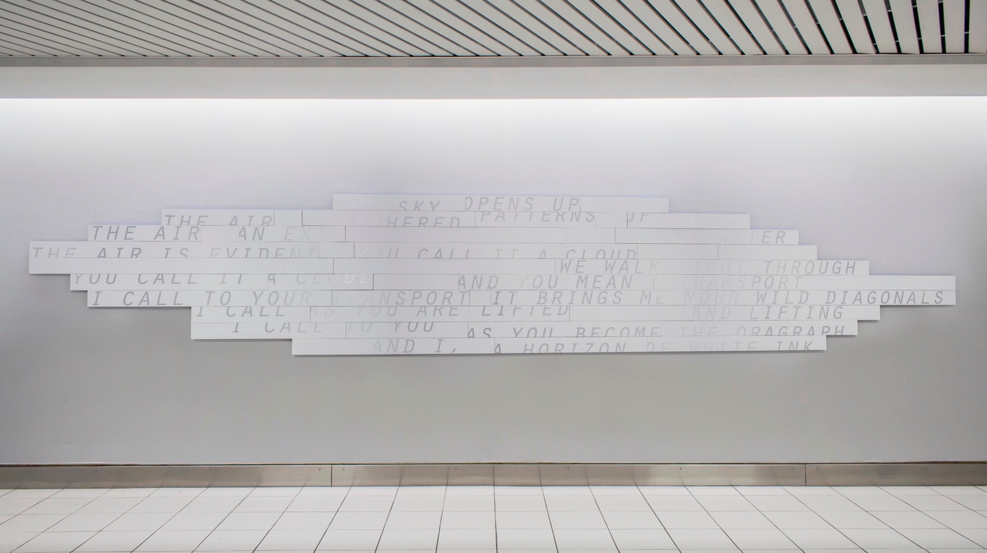 Installation on a white wall: long, thin white panels are tiled to form a geometric cloud-like shape; some of their surfaces are printed with slightly offset text, set in a light all-caps sans serif font.