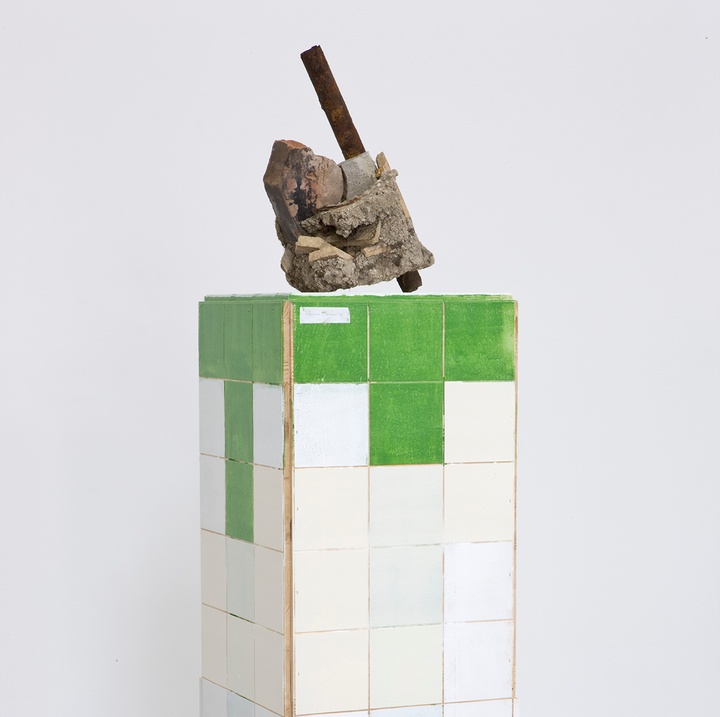A piece of construction materials (concrete, rebar) sits atop a pillar made of white and green tiles