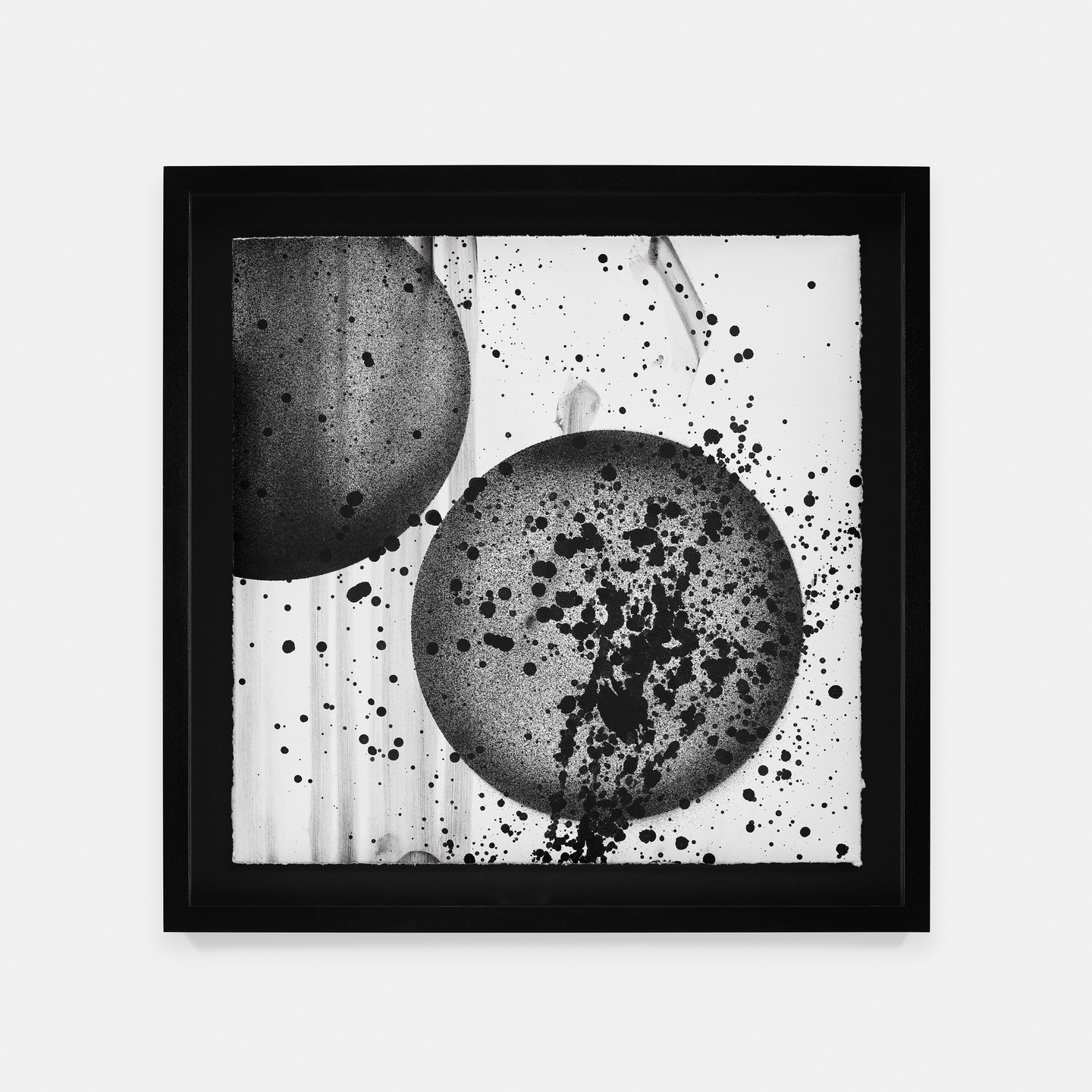 A square, black frame surrounds two gray circles with splatters of black ink on them and on the white ground