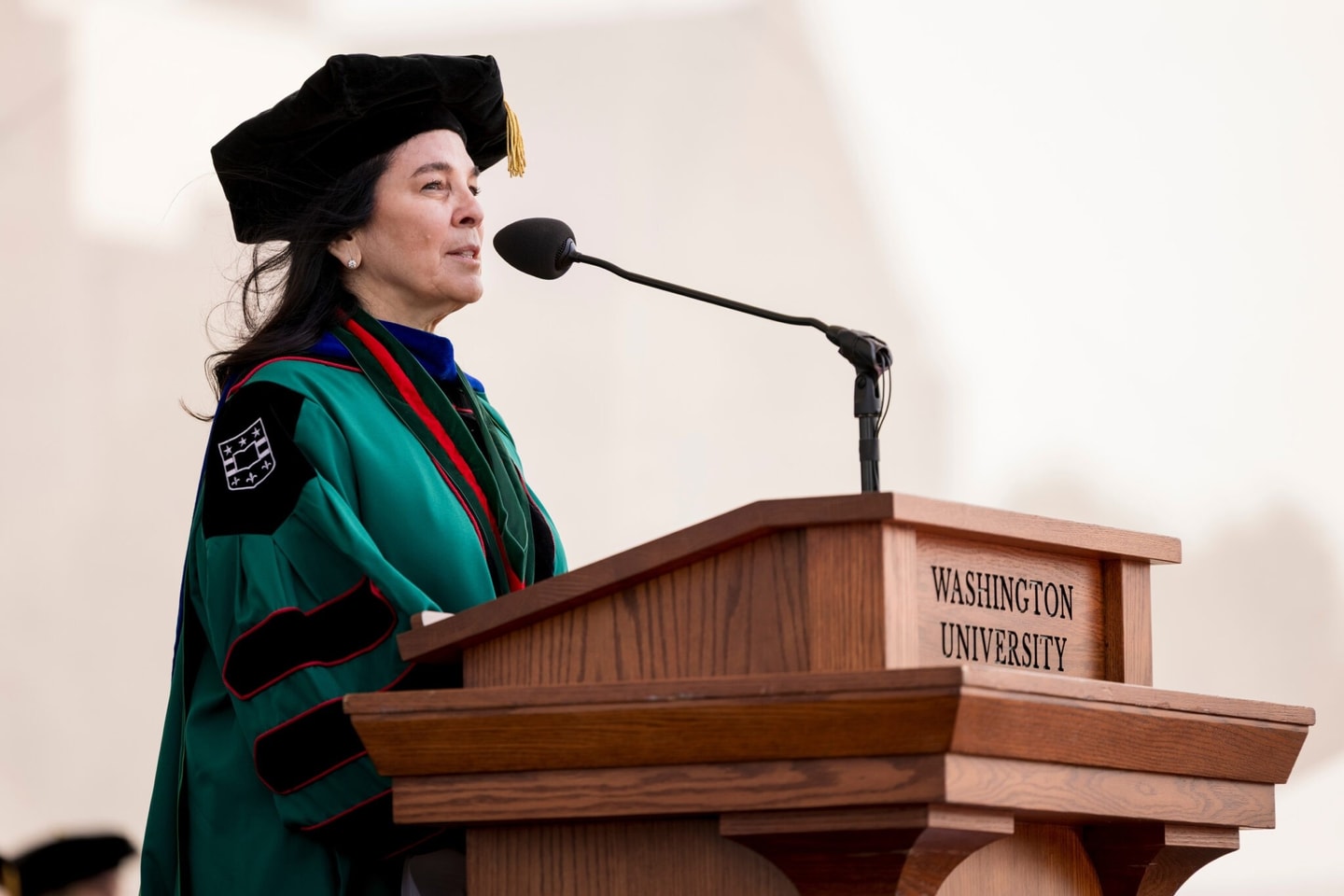 Vicki Match Suna dressed in commencement robe standing at a podium speaking