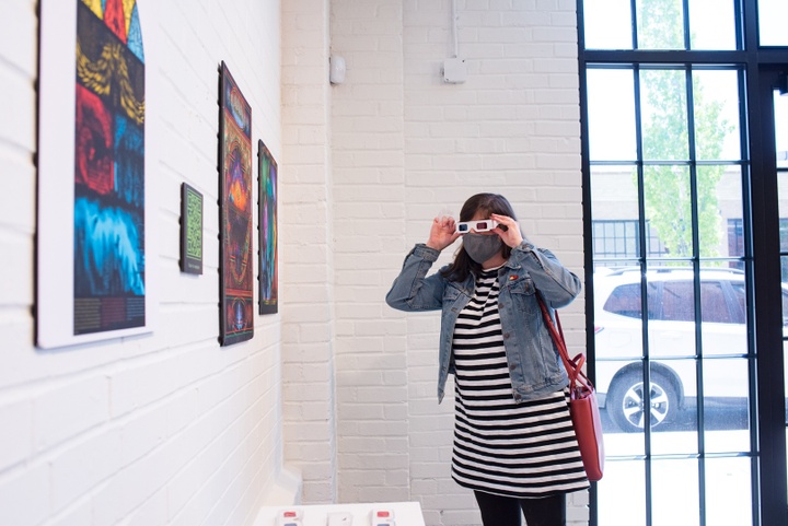 Person in 3D glasses looks at three prints on a white wall.