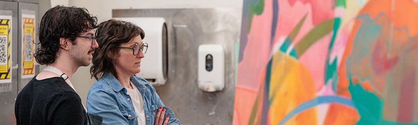 A female professor and a male student look at a painting together
