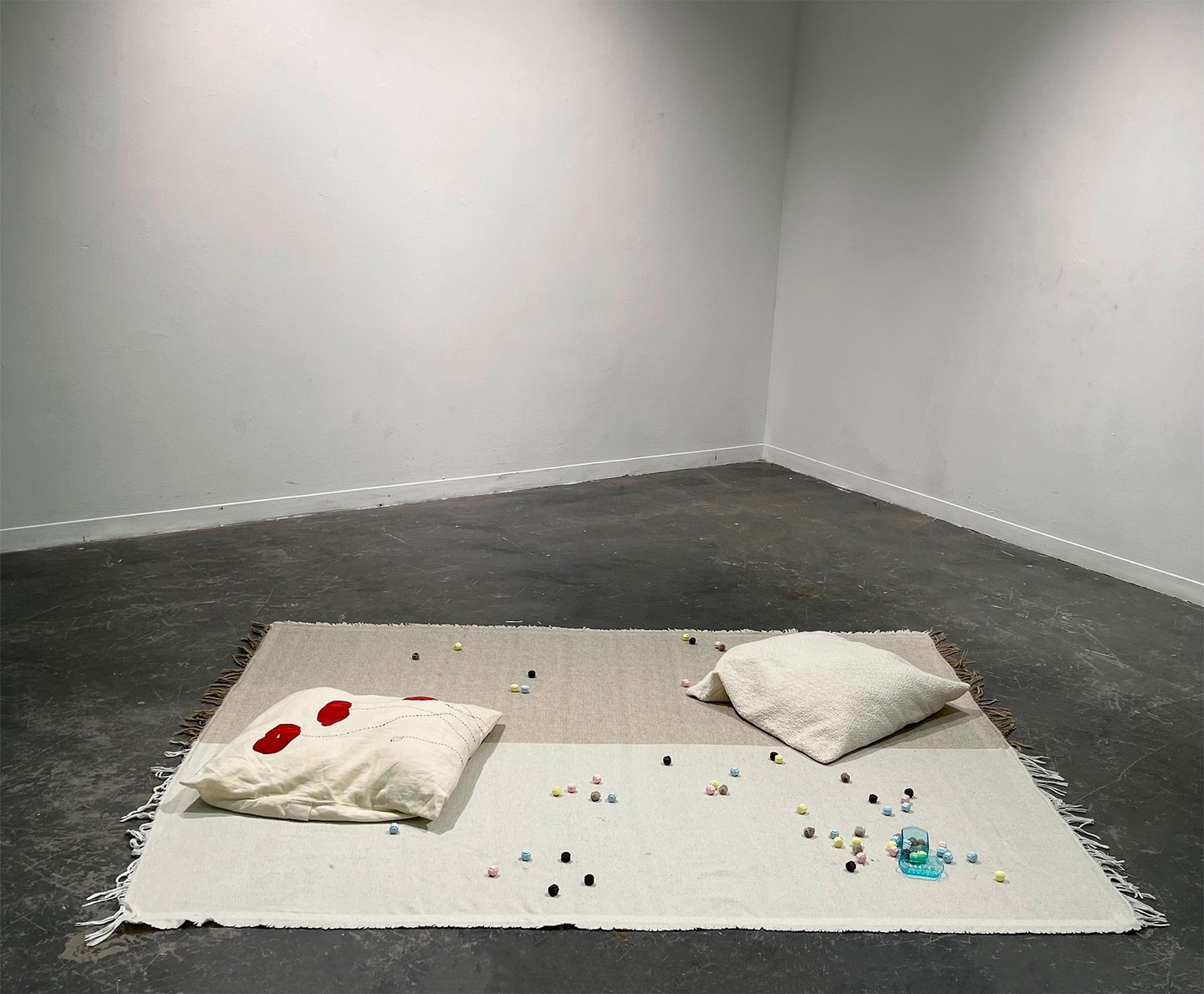 a sculpture comprised of two pillows, one embroidered with flowers and there are little colorful bits scattered around them.