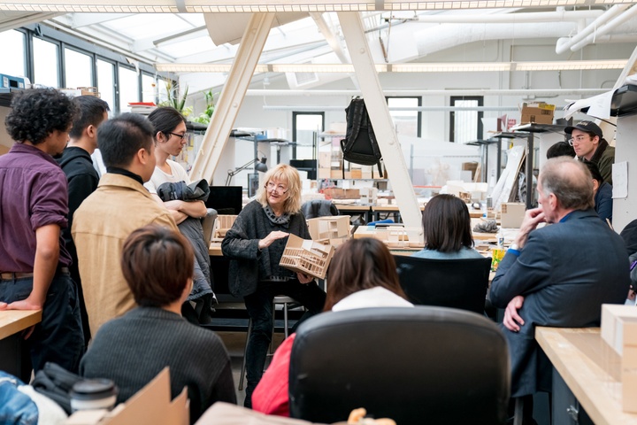 Top-floor studio space with full skylights and exposed I-beams and an open desk area that allows for a small gathering of people listening to an instructor.