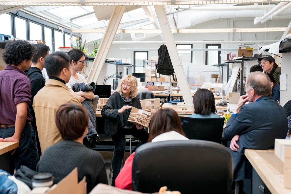 Top-floor studio space with full skylights and exposed I-beams and an open desk area that allows for a small gathering of people listening to an instructor.