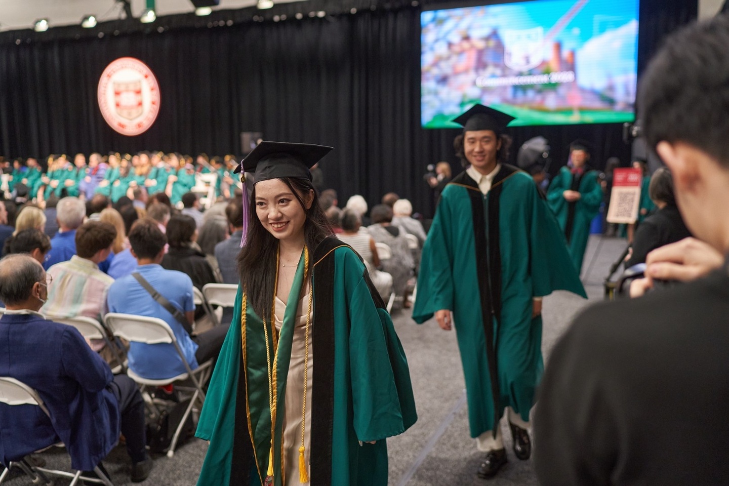 Students in green graduation robes and caps process down an aisle at the recognition ceremony.