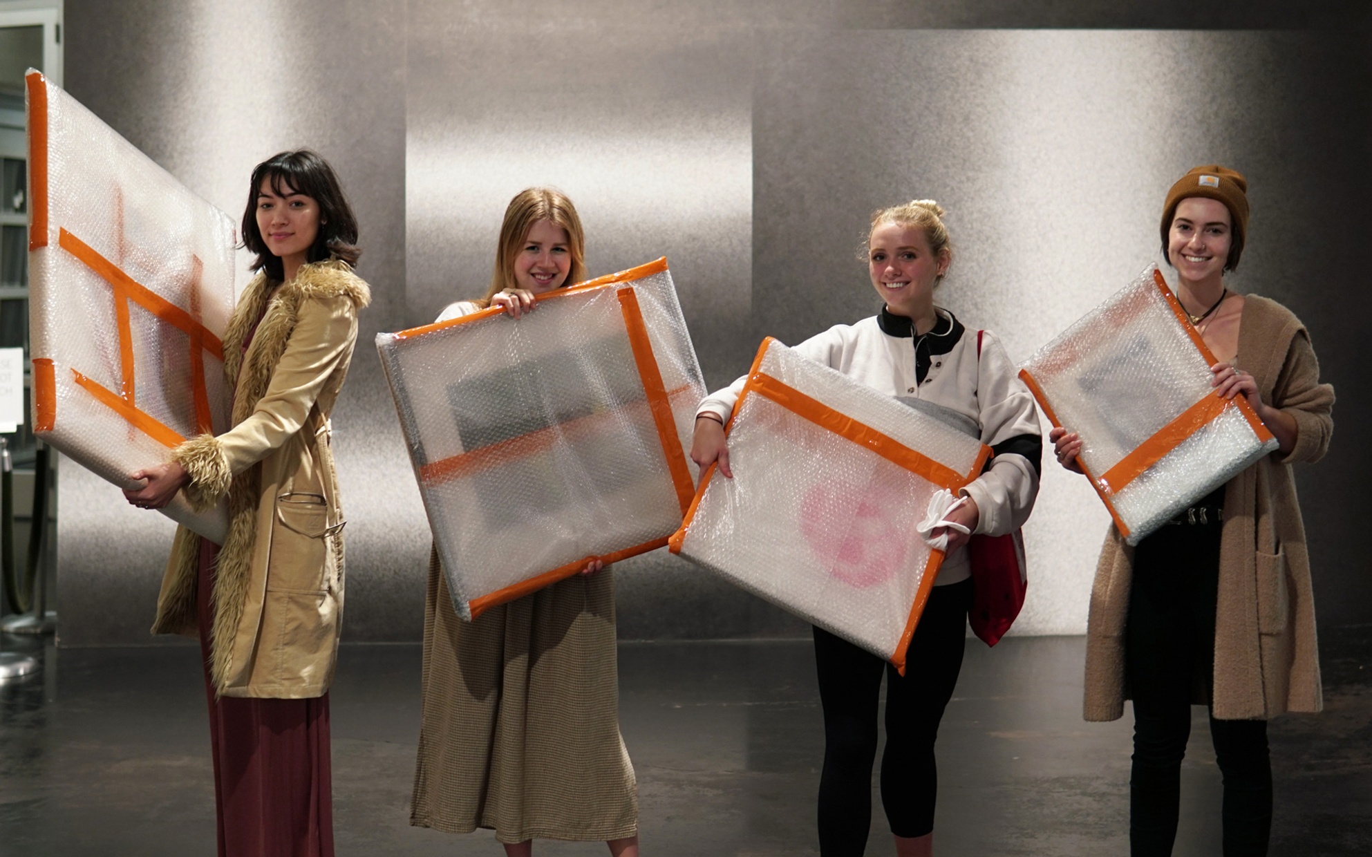 four smiling students stand and pose with their wrapped and framed artworks before leaving the museum to bring the works home for the semester
