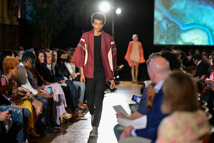A model walking down the runway in black pants and black shirt with a red kimono-style jacket