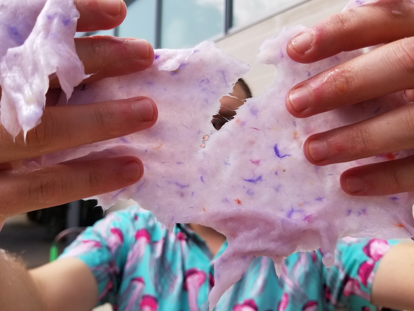 Hands pulling apart gooey pink, stretch paper pulp.