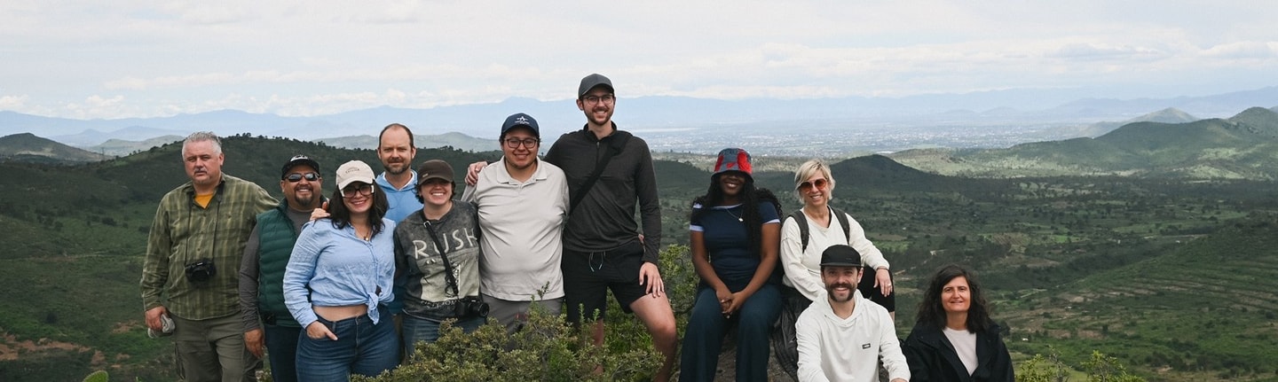 A group of people stand on a mountain top smiling at the camera with a valley behind them