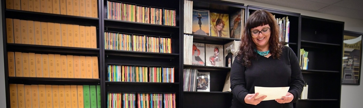 Person looks at original golden age illustration in her hands. Library stacks with periodicals can be seen behind them.