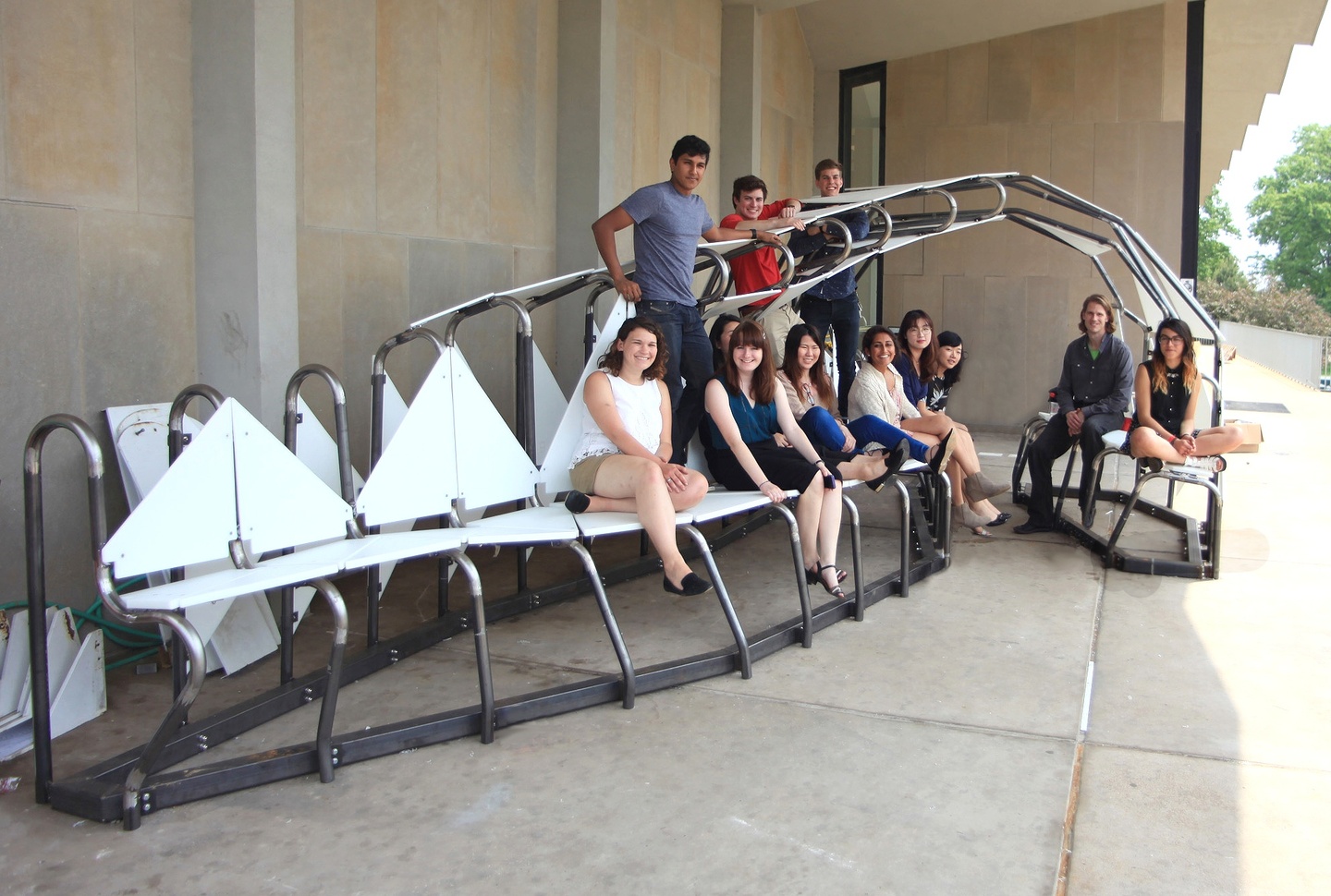 A group of people sit on a white and metal seating structure. 
