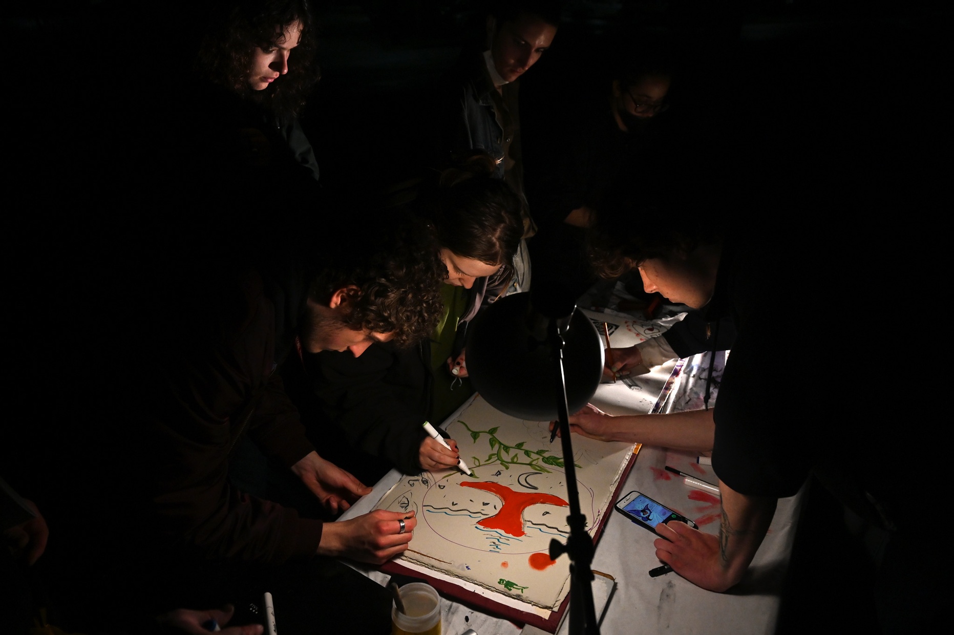 Multiple people gather around a large book to draw on it.