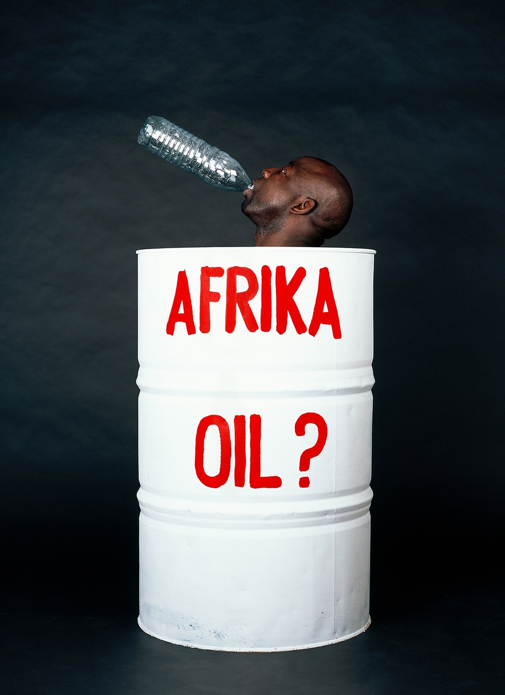 A large white barrel says “AFRIKA OIL?” on it in red and a black man’s head leans out of the top with a plastic bottle in his mouth.