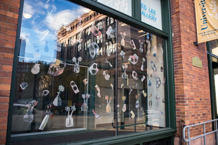 Front window of a gallery with a collection of small flower-shaped cutouts attached to the inside of the glass.