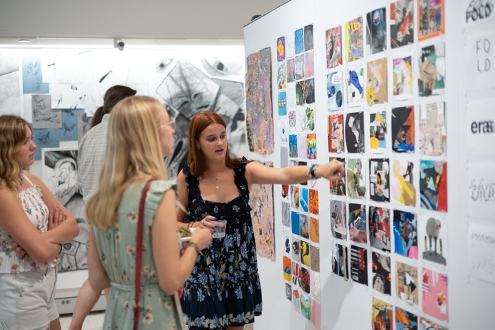 Two students look at a wall of art at an exhibition.