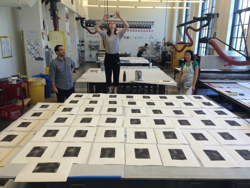 Prints with rectangular black squares in the middle of them laid out across the tables for drying