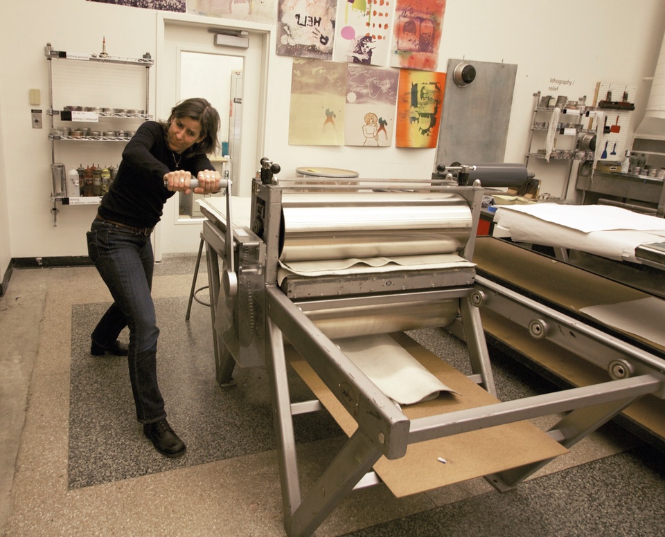 Nina Katchadourian cranking the large printing press with two hands 