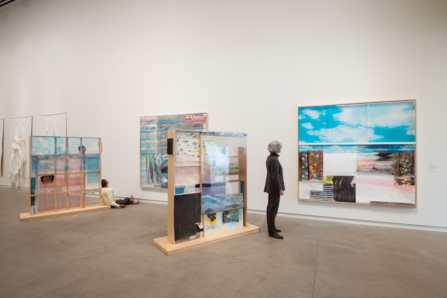 A gallery view of two large rectangular sculptures in front of two wooden frames with an assemblage of materials