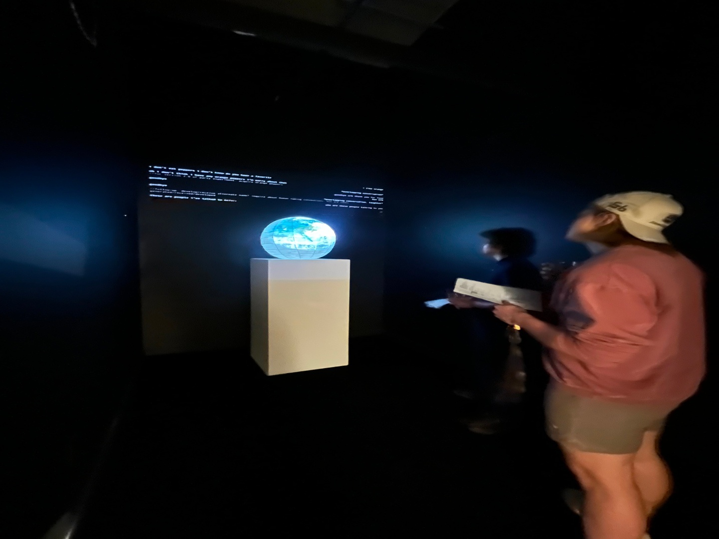 A photo of a person looking at an orb on a pedastal bathed in light in fron of a wall of text.