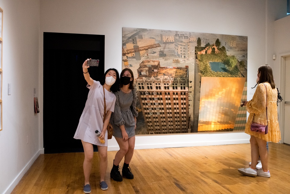 Two students take a selfie in front of a large wall print