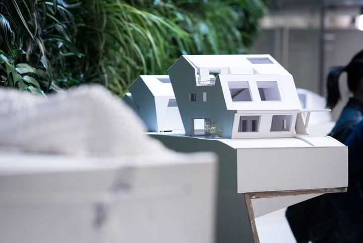 Shot of a white house-like building model displayed against a living green wall.