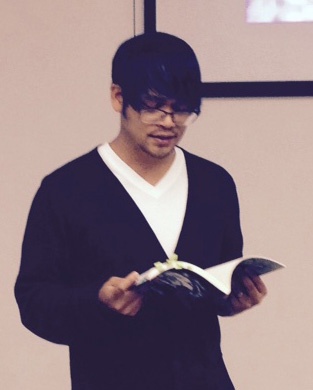 A photo of Paolo Javier holding a book open and looking down at it as if reading. 