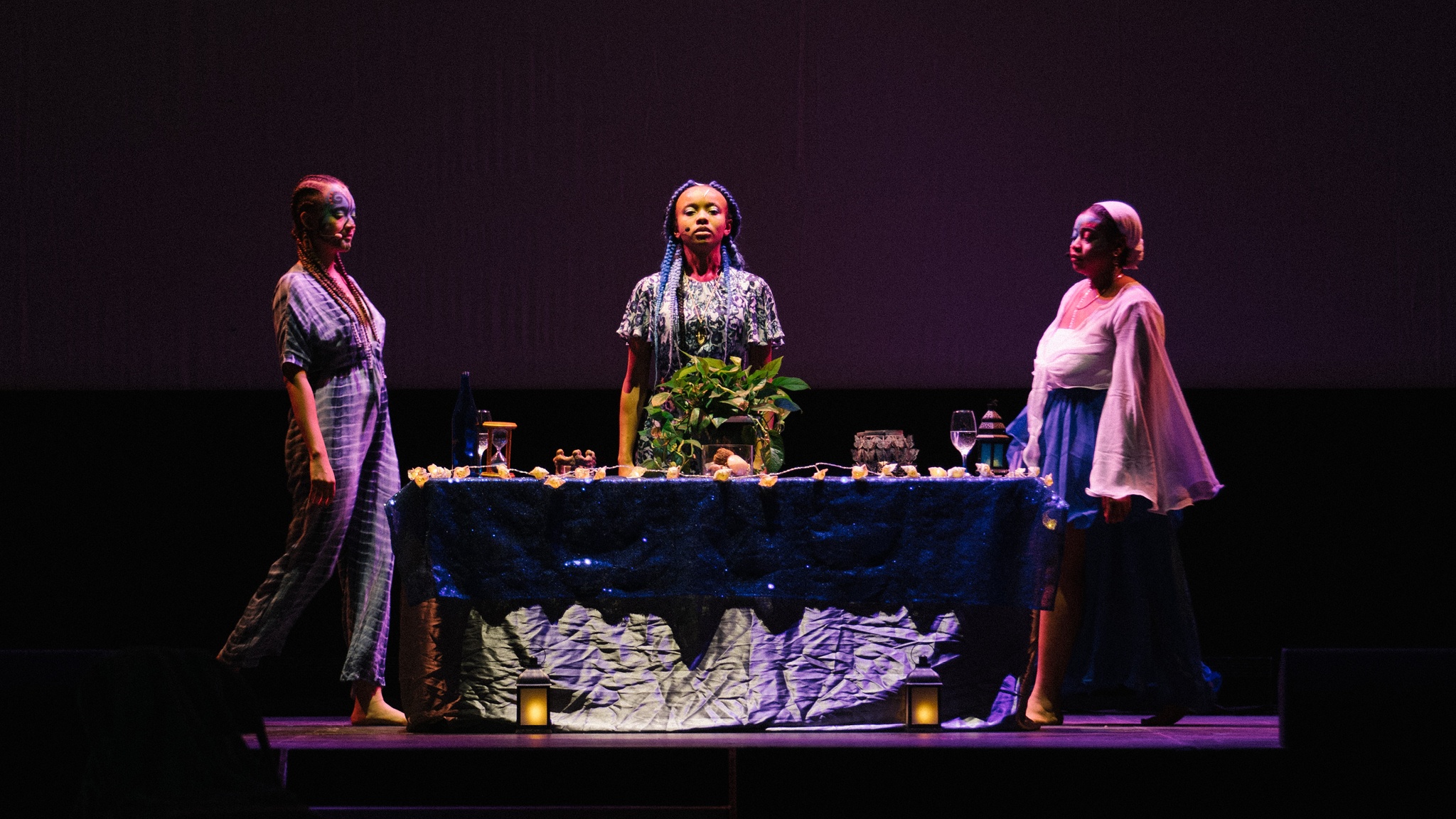 Three performers stand around a table resembling an altar that is illuminated by dramatic stage lighting