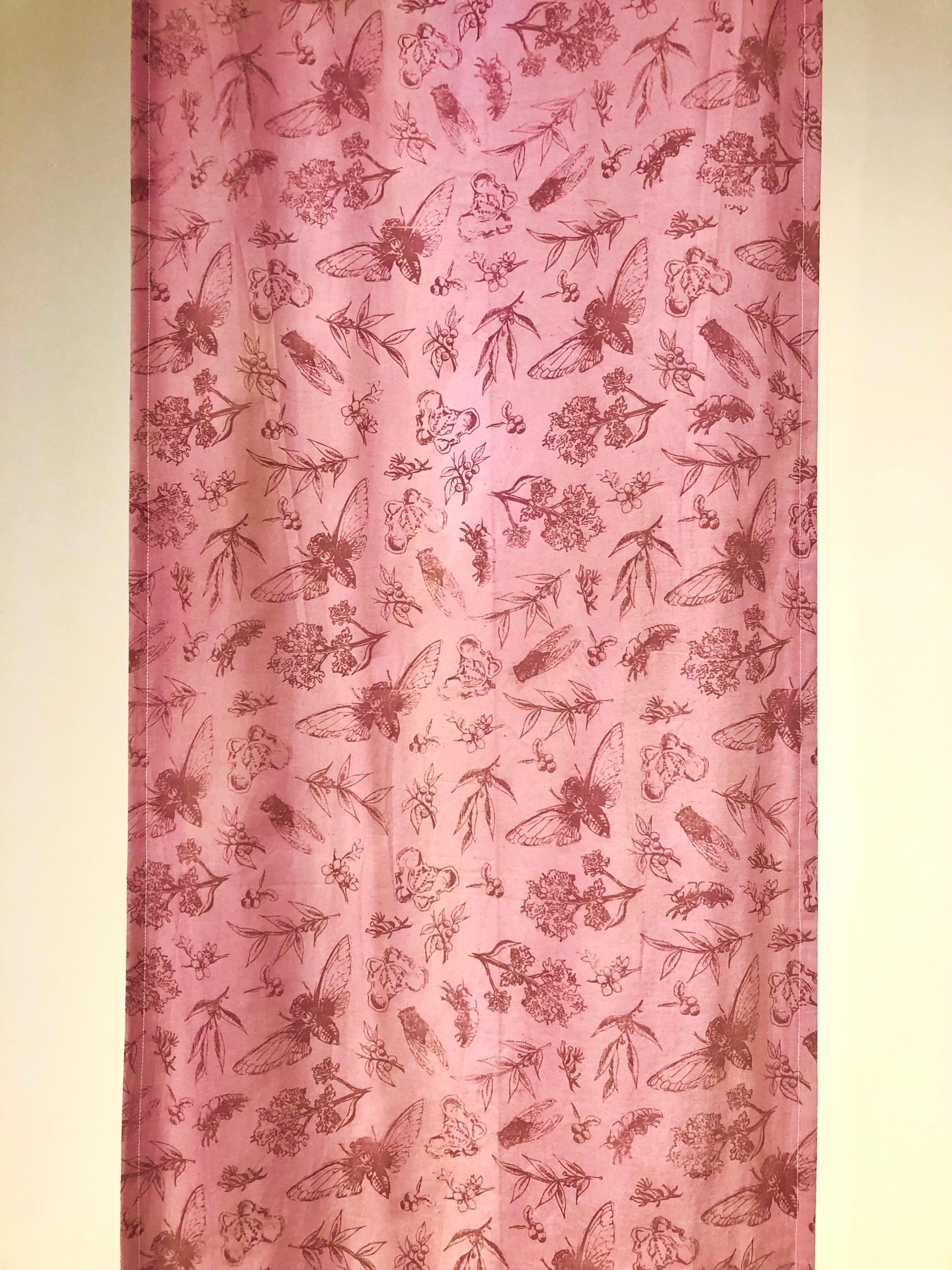 A pink tapestry with bugs leaves and bones printed on it.