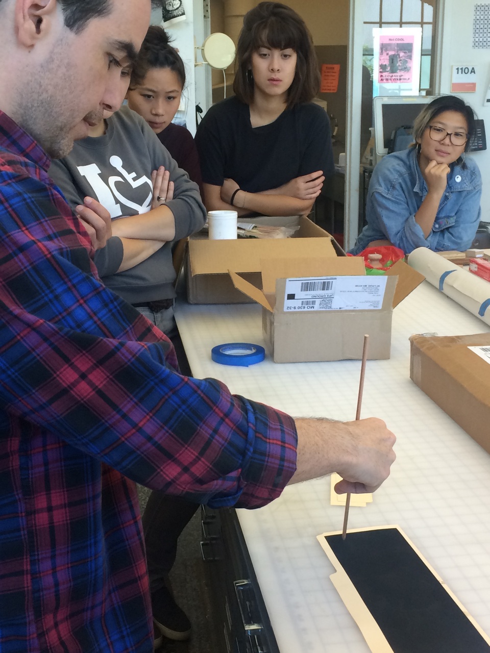 Dario Robleto doing a demonstration to students with a pencil on a narrow sheet of black paper