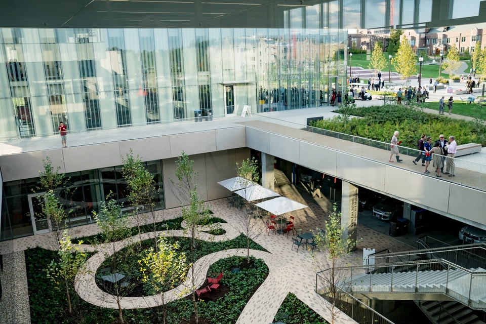 Recessed area next to a low glass walled building and a park that has a winding brick path and shade plants.