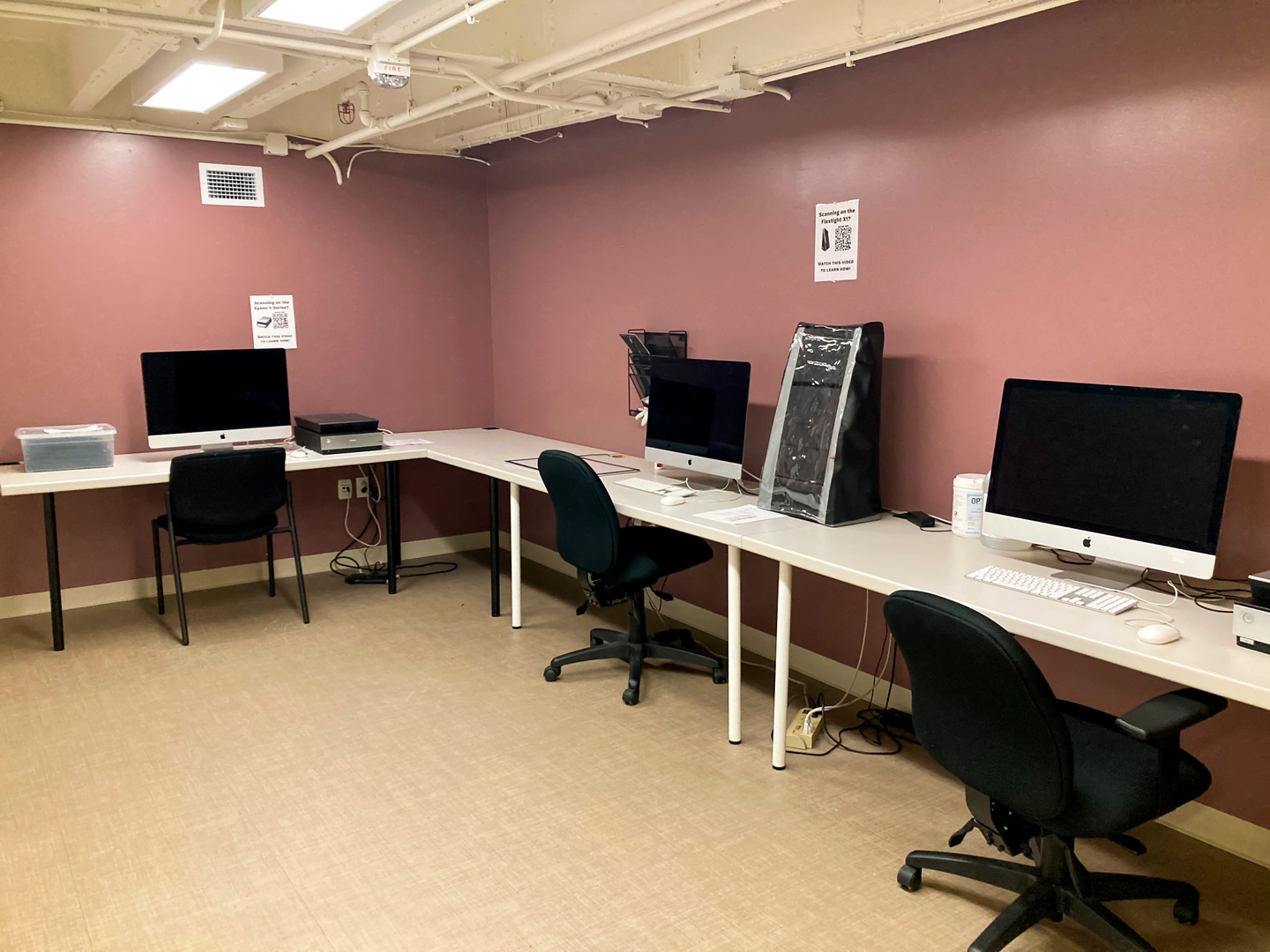 Room with bright green walls and long tables on each side with several printers sitting on top.