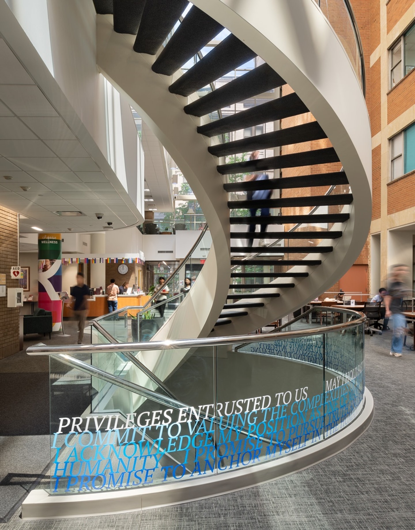 A curving staircase with glass sides and the hippocratic oath installed in blue vinyl