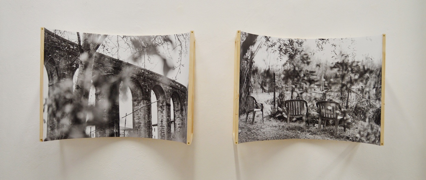 Two black and white photographs of an ancient aqueduct and a backyard with lawnchairs, both affixed to concave boards.